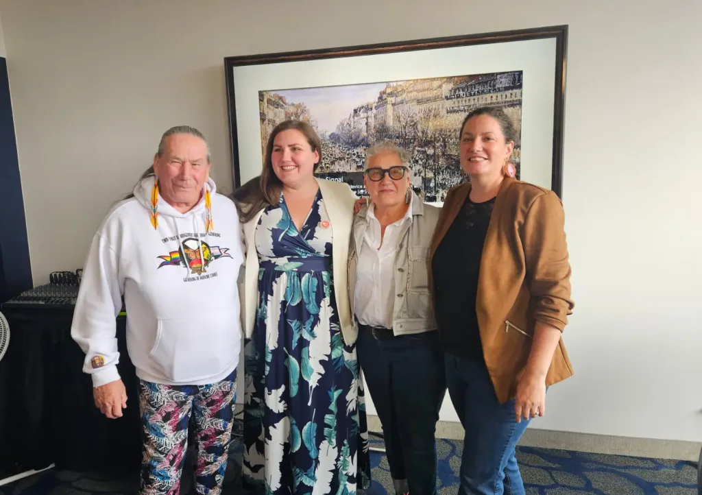 A group of people stand together in front of a large painting posing for a photo